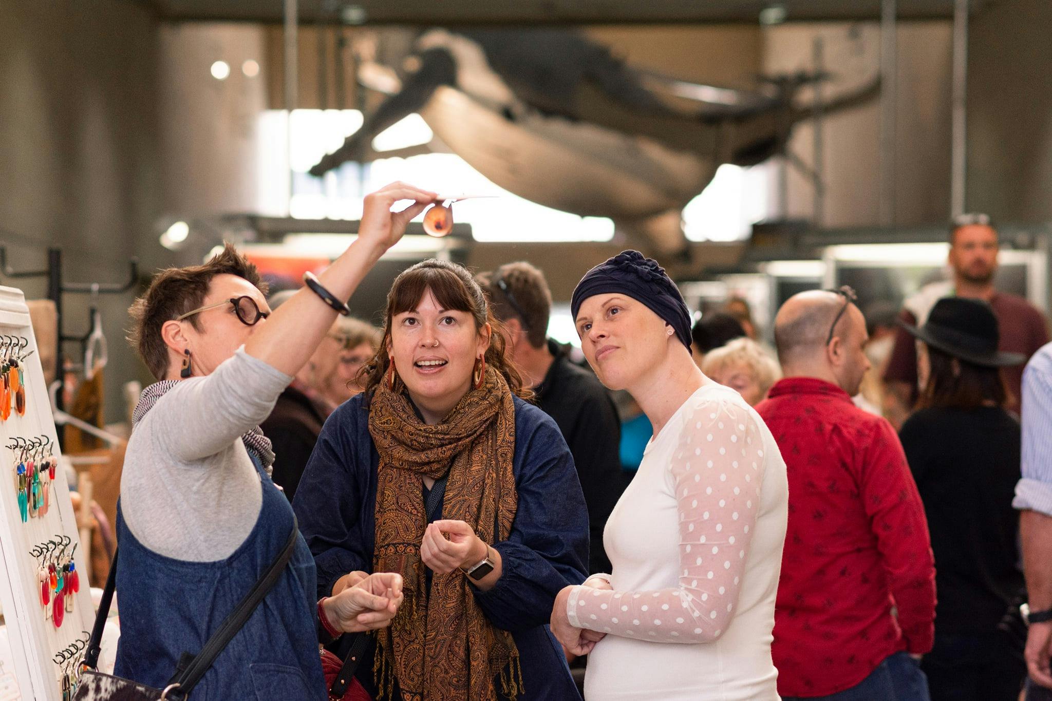 Stallholders shows shoppers the colours in handmade earrings by holding it up to the light
