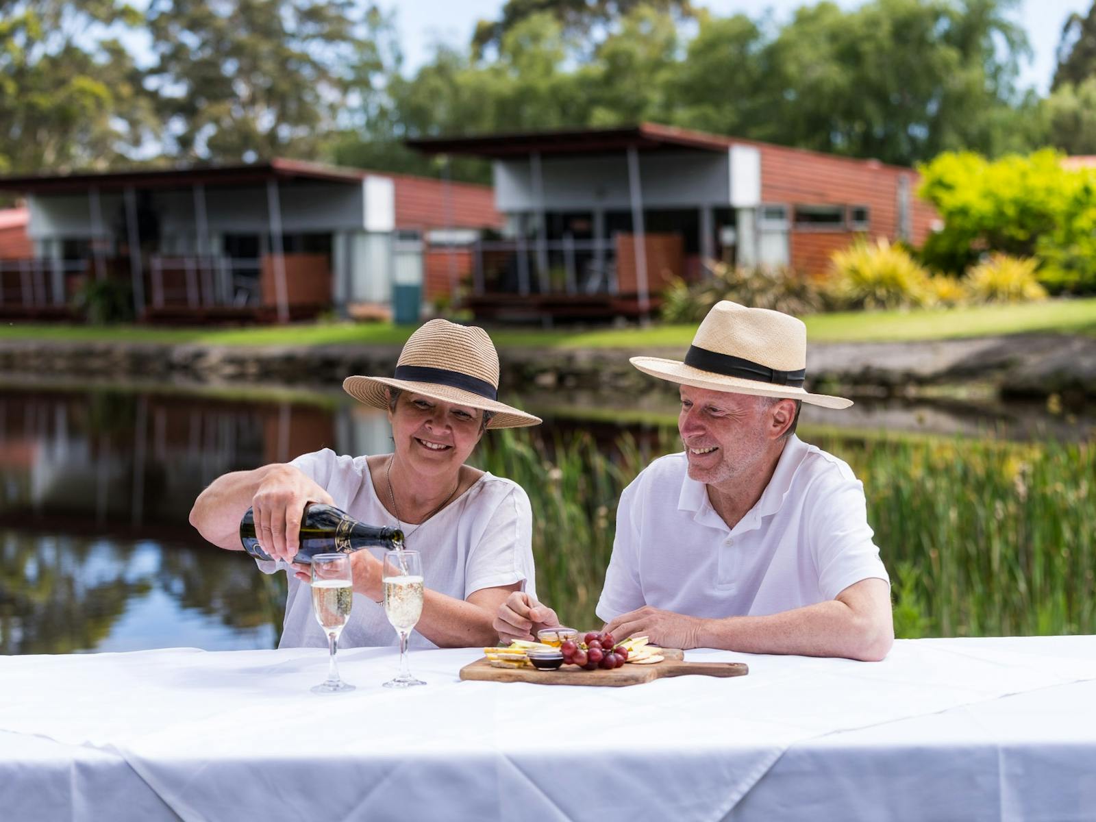 Couple sharing sparkling wine and cheese platter on outdoor picnic table on the edge of the lake