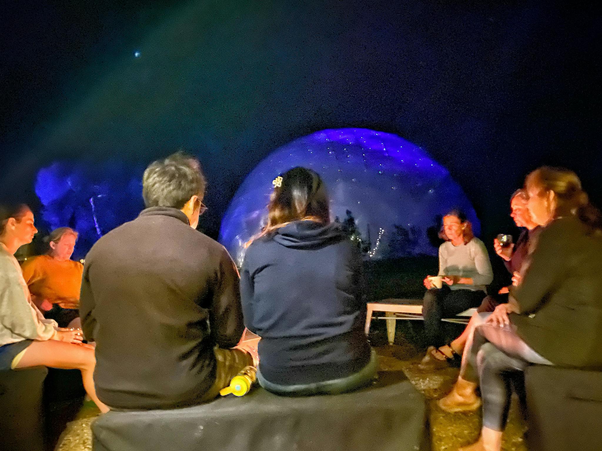 People sitting around fire pit in front of meditation dome