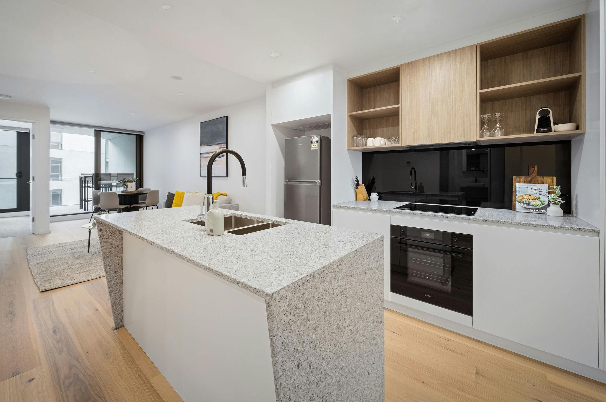 Modern, spacious apartment kitchen with island bench, oven, stovetop and wood-look floors.