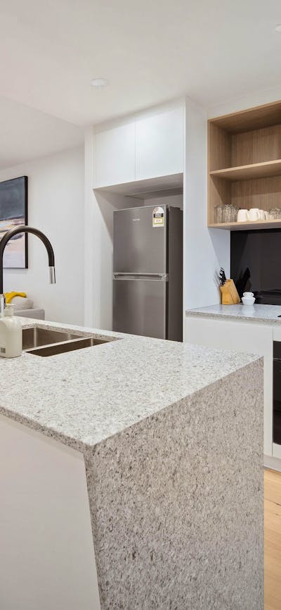 Modern, spacious apartment kitchen with island bench, oven, stovetop and wood-look floors.