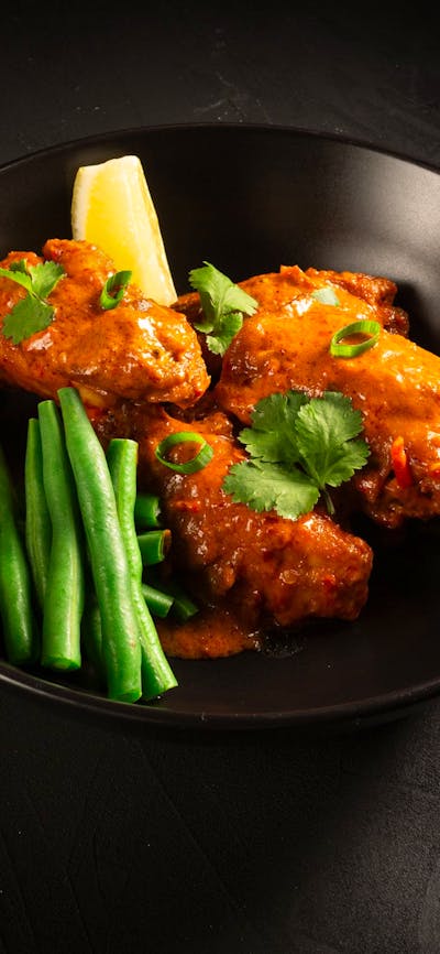 Ayam Rujak with green beans served on a black plate with a lemon wedge