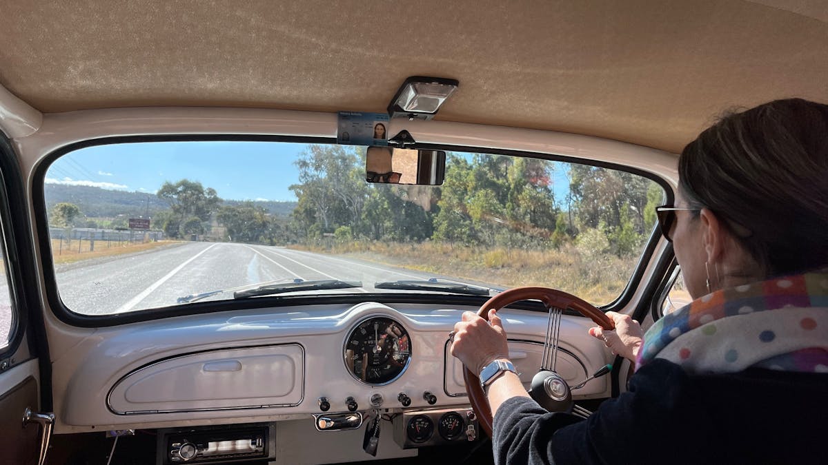 inside view of a vintage car, driver at the wheel and open country roads ahead