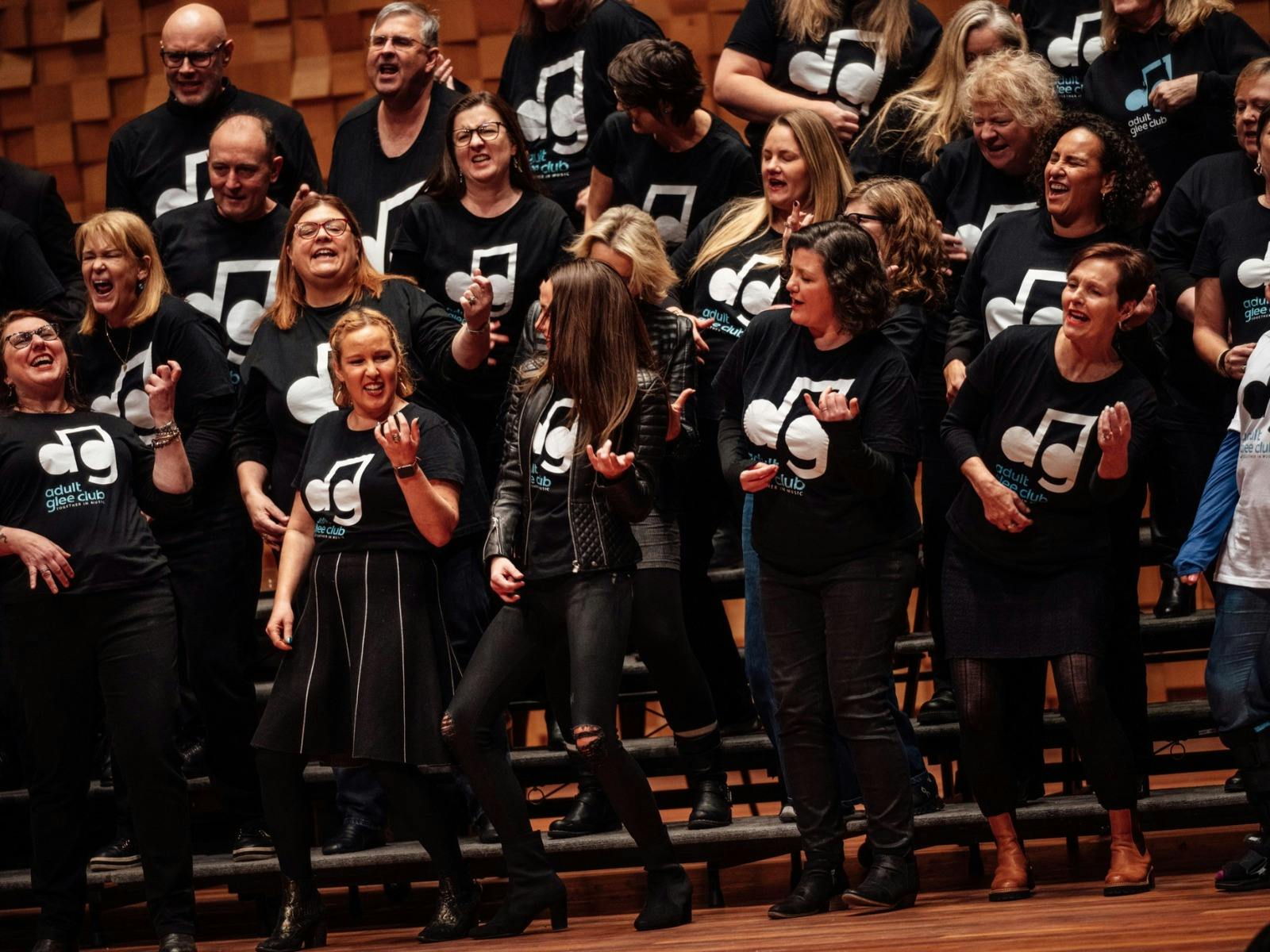 A large choir, wearing black "Adult Glee Club" shirts, singing and gesturing.