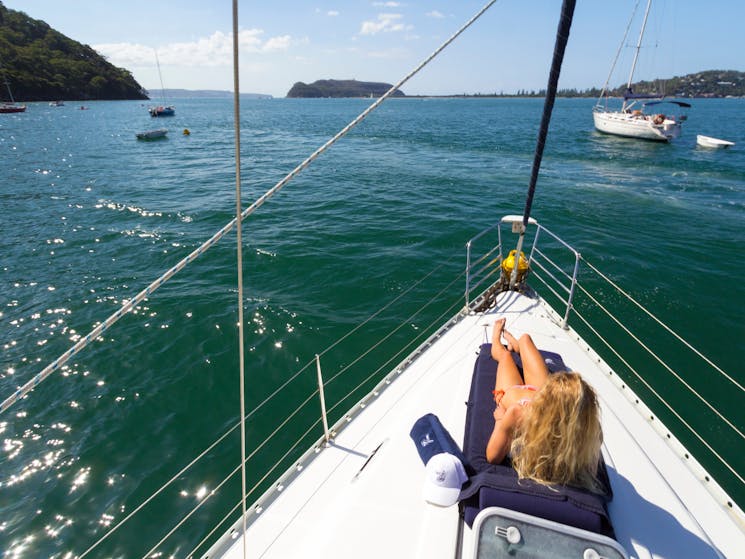 Lady relaxing on sunlounge on the bow of Taylor Made  Escapes yacht in beautiful Pittwater, Sydney