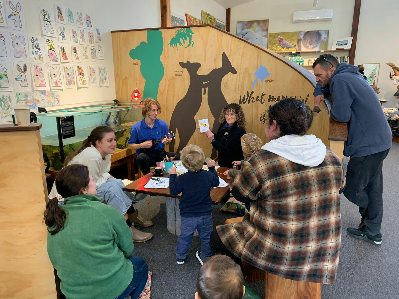 A man playing the ukelele and a woman reading a book to a group of kids