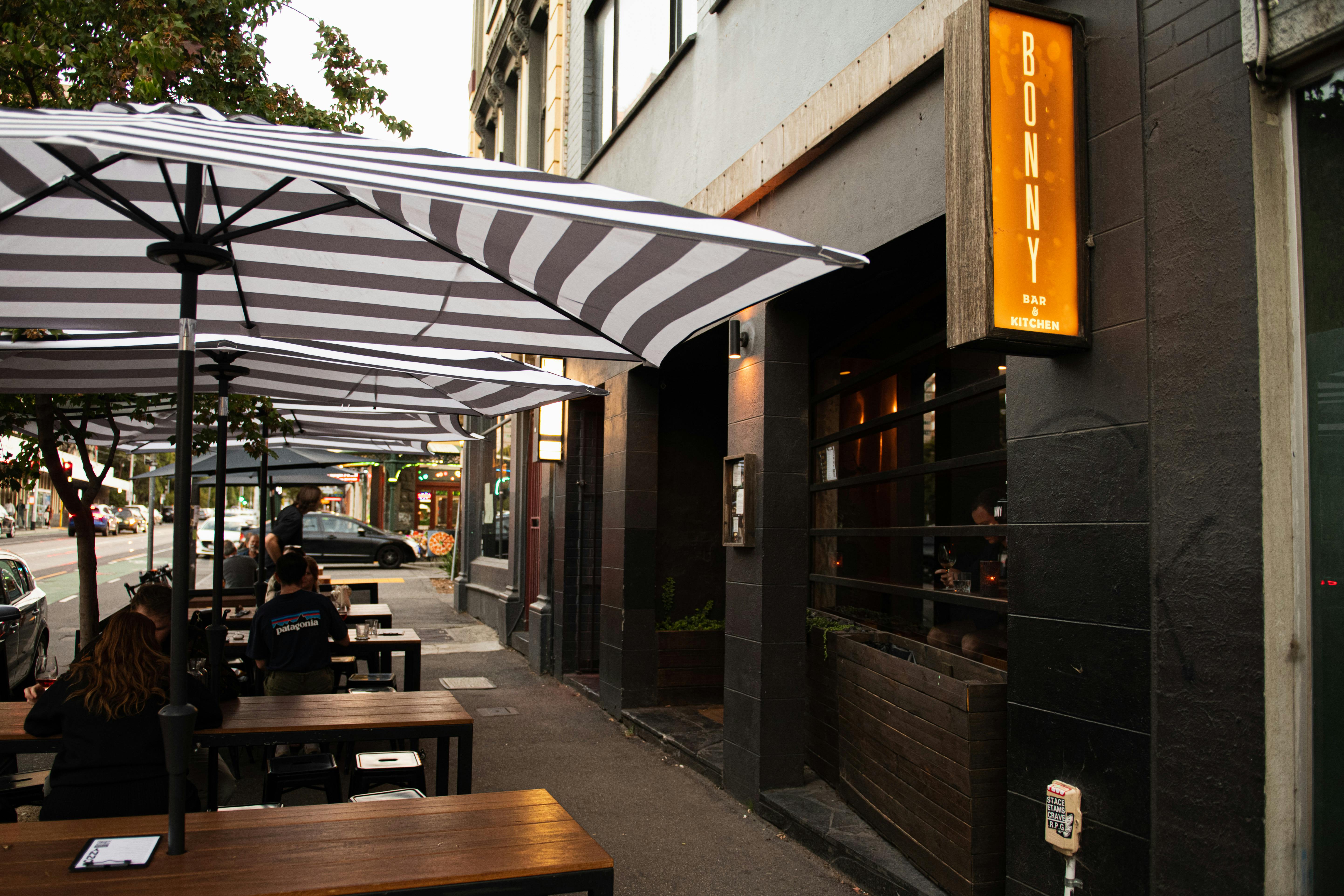 A view of the exterior of Bonny Bar with footpath tables and umbrellas .