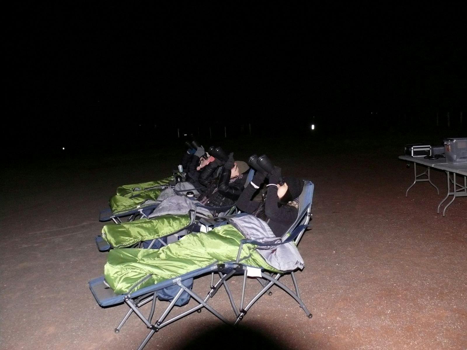 Girls in reclined chairs in sleeping bags using binoculars