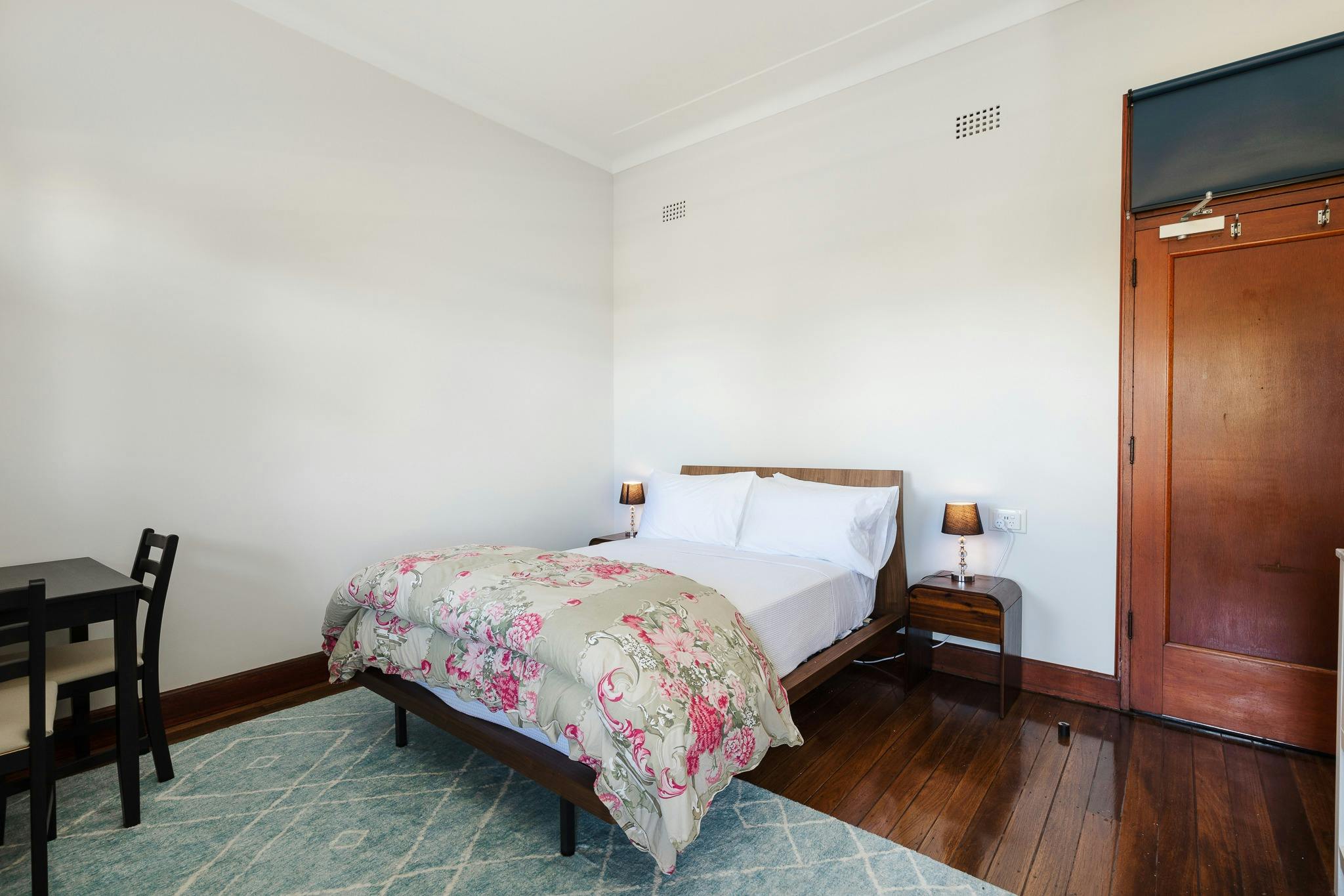 Queen bed in spacious room polished floor white sheets table chair