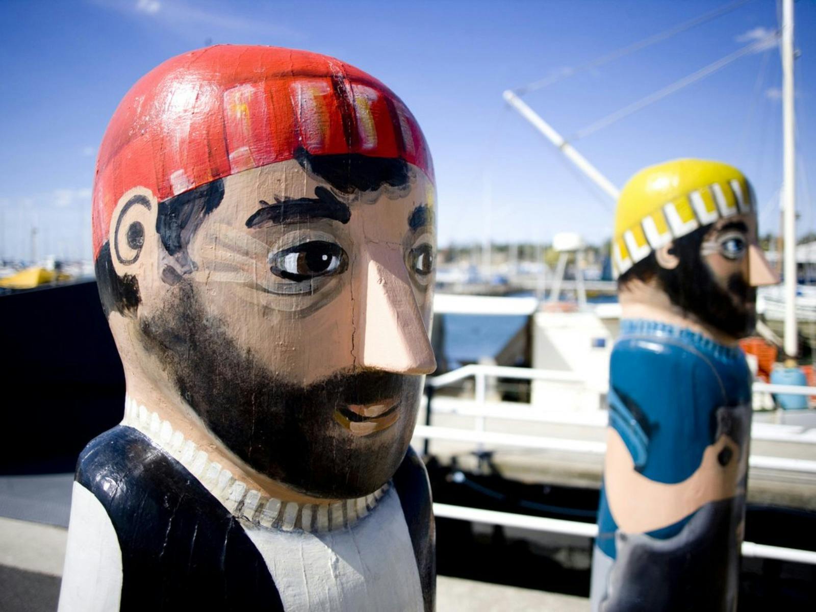 Two fisherman painted on bollards on waterfront dock
