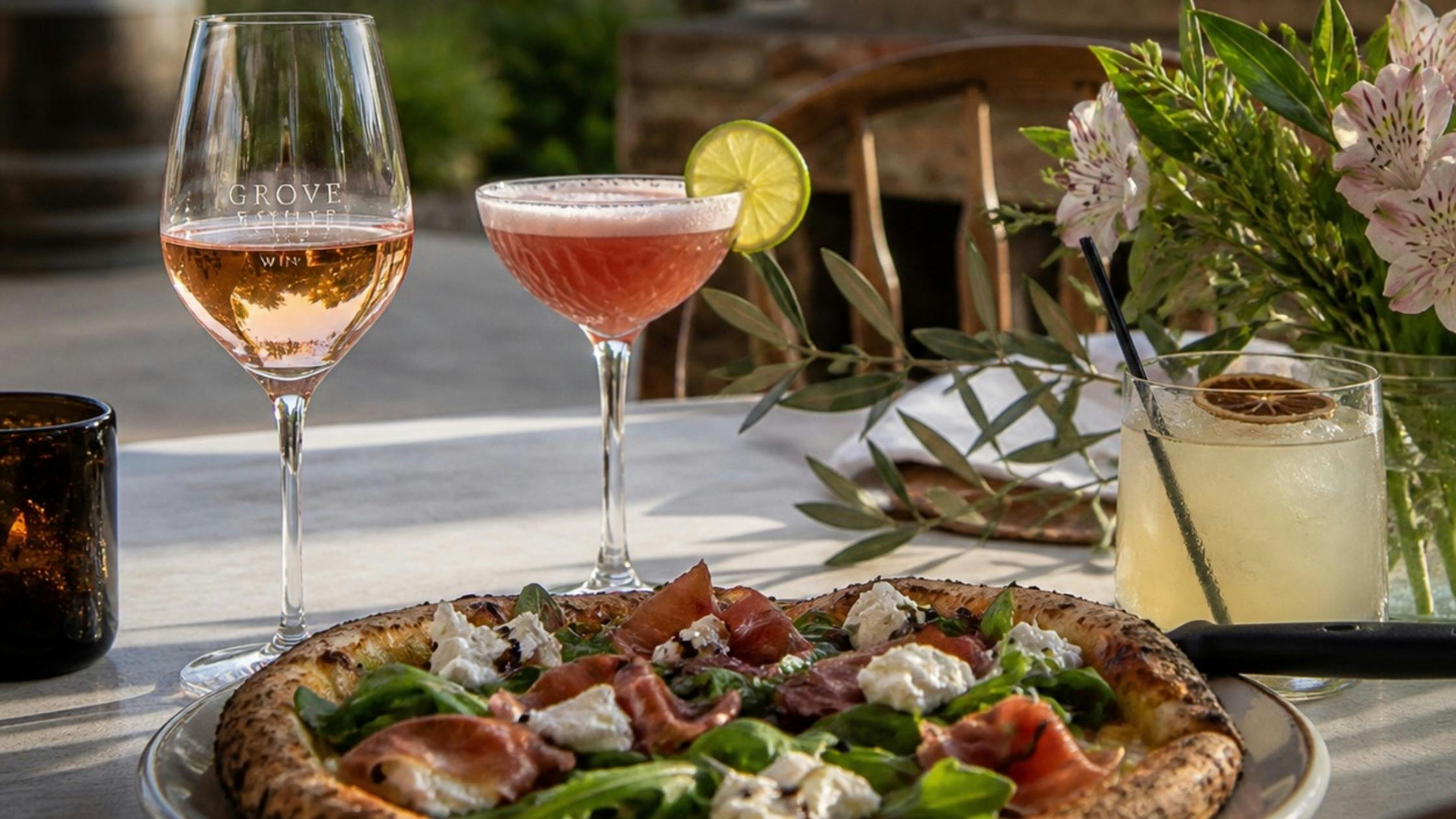 Glass of wine, cocktail and wood fired pizza on table