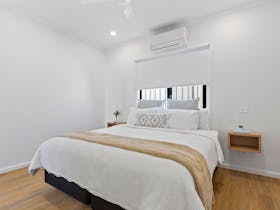View of double bed, pillows, bedside tables, mustard coloured throw, airconditioner.