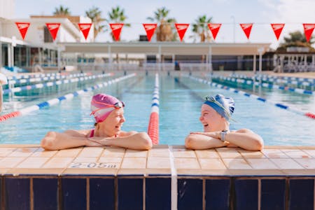 Two swimmers perched up on the edge of the pool smiling at each other