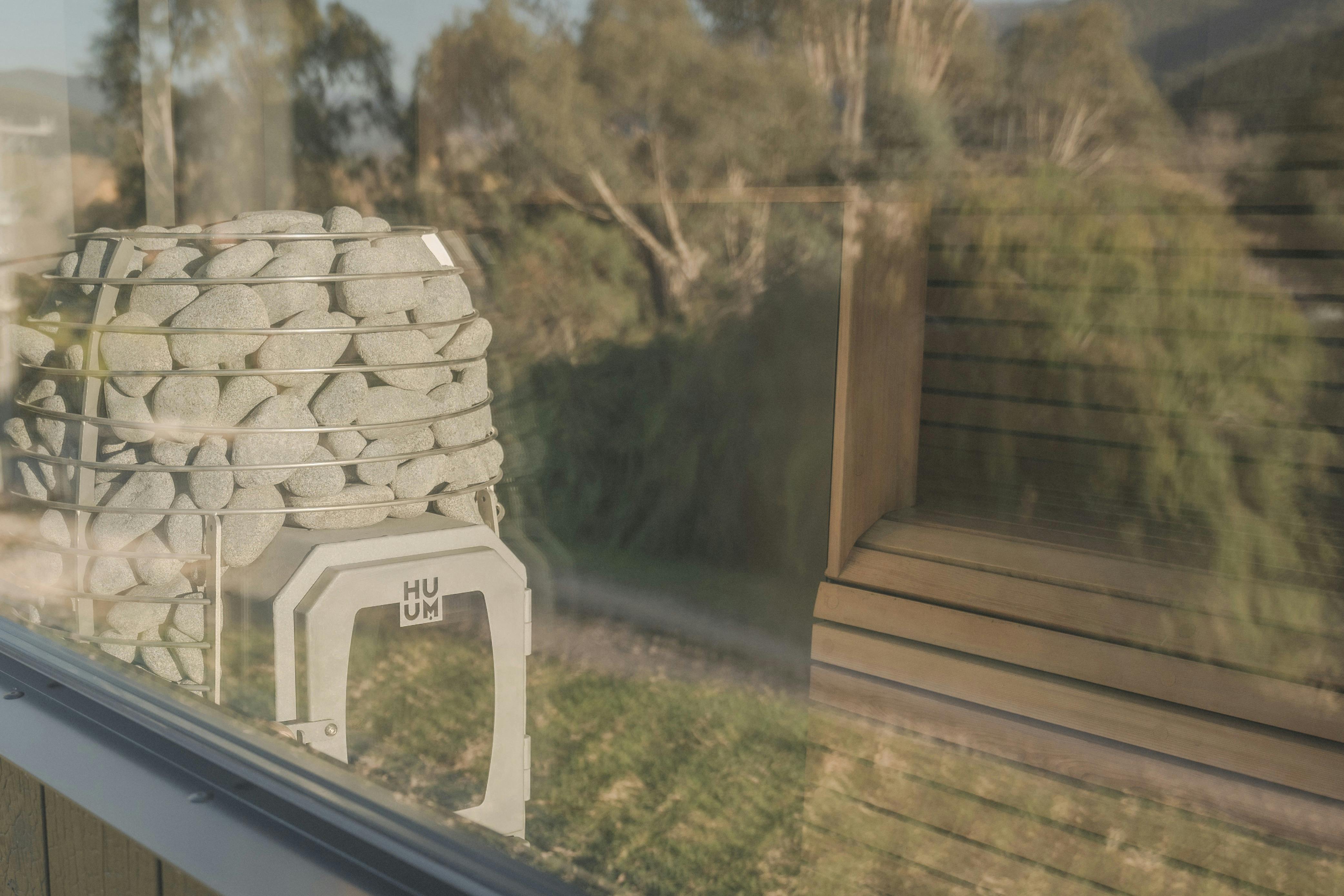 Reflection of nature on outside of sauna glass looking into sauna heater and cedar bench