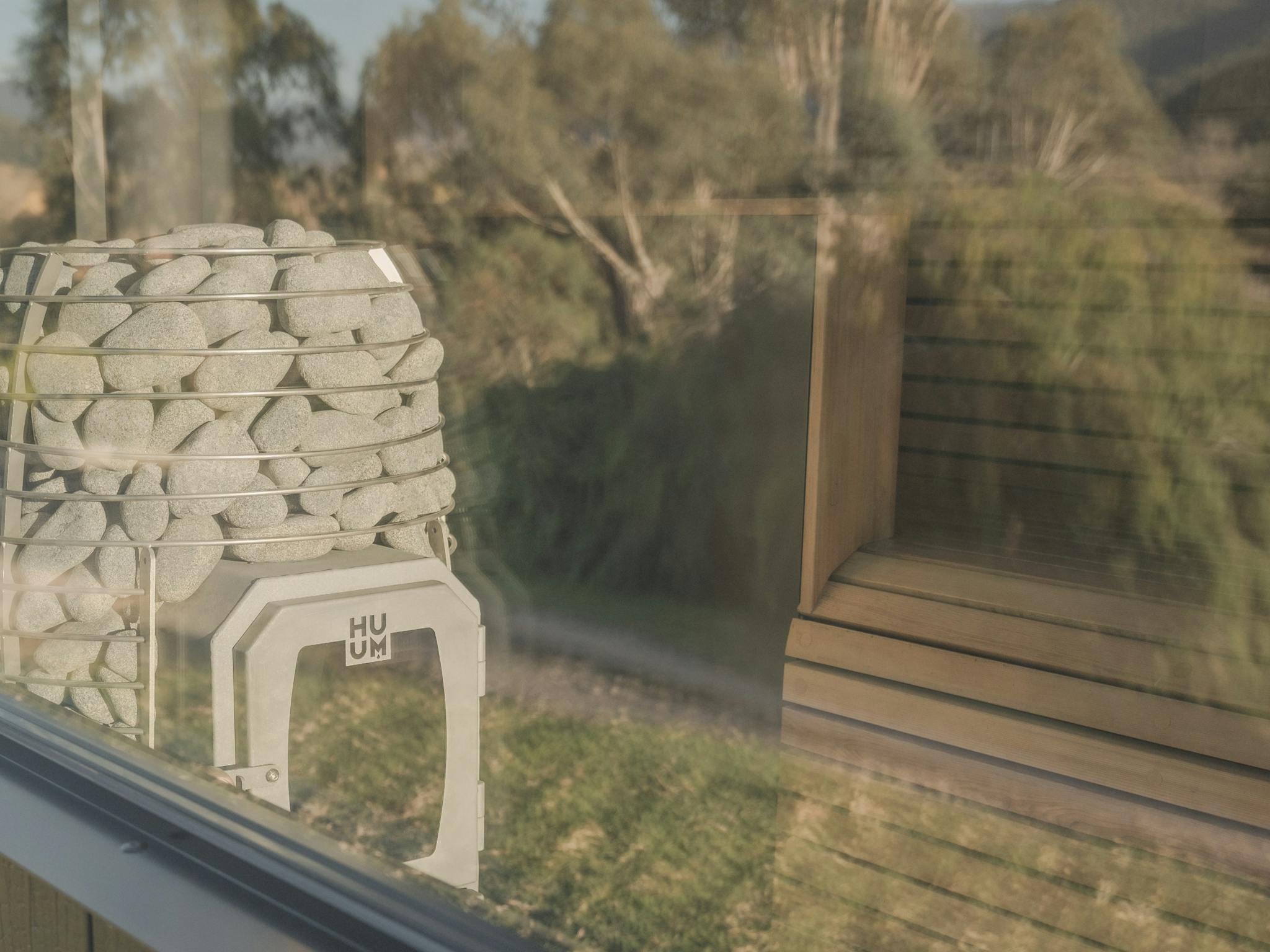 Reflection of nature on outside of sauna glass looking into sauna heater and cedar bench