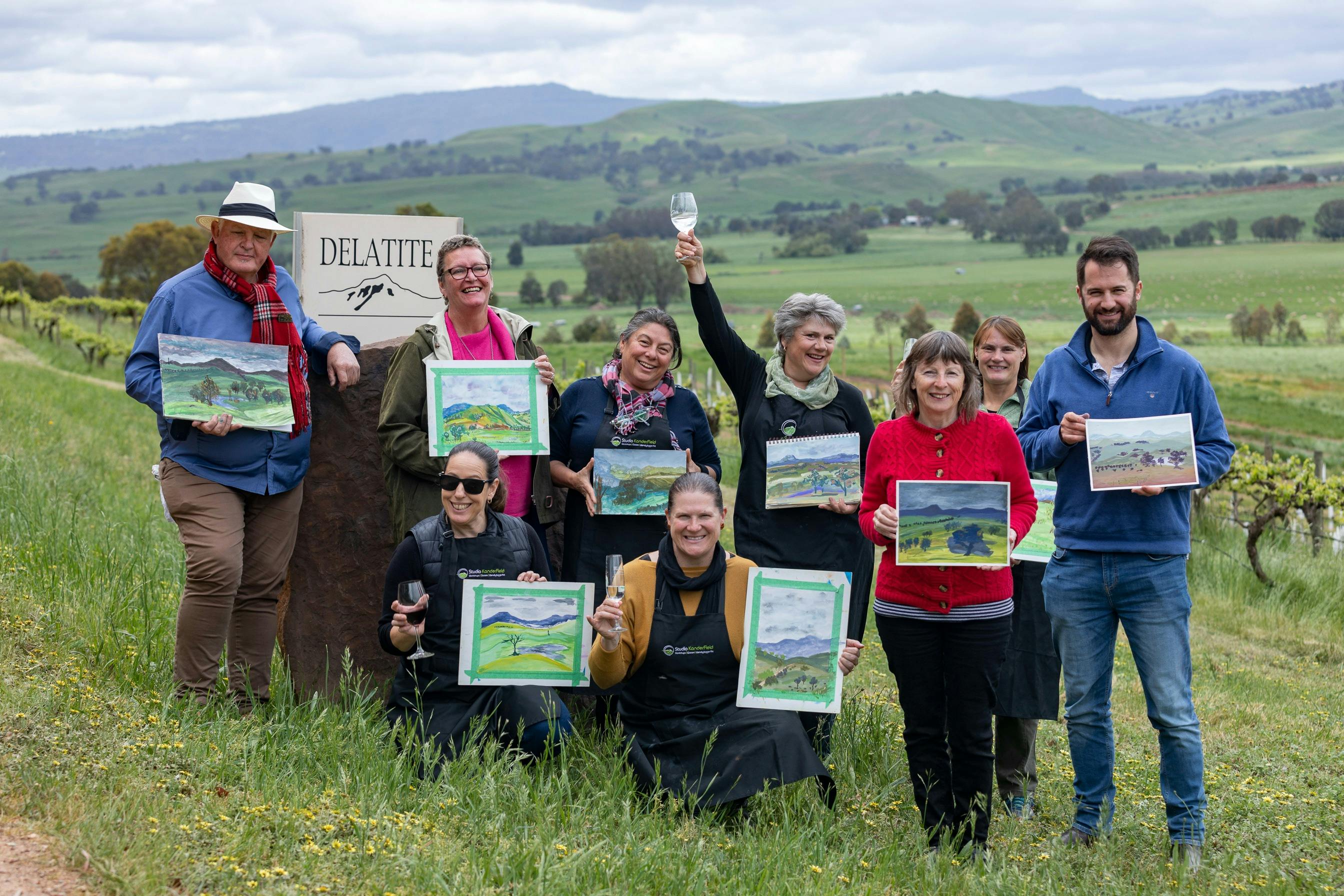 artists display their paintings, mountain views behind them, and vineyard
