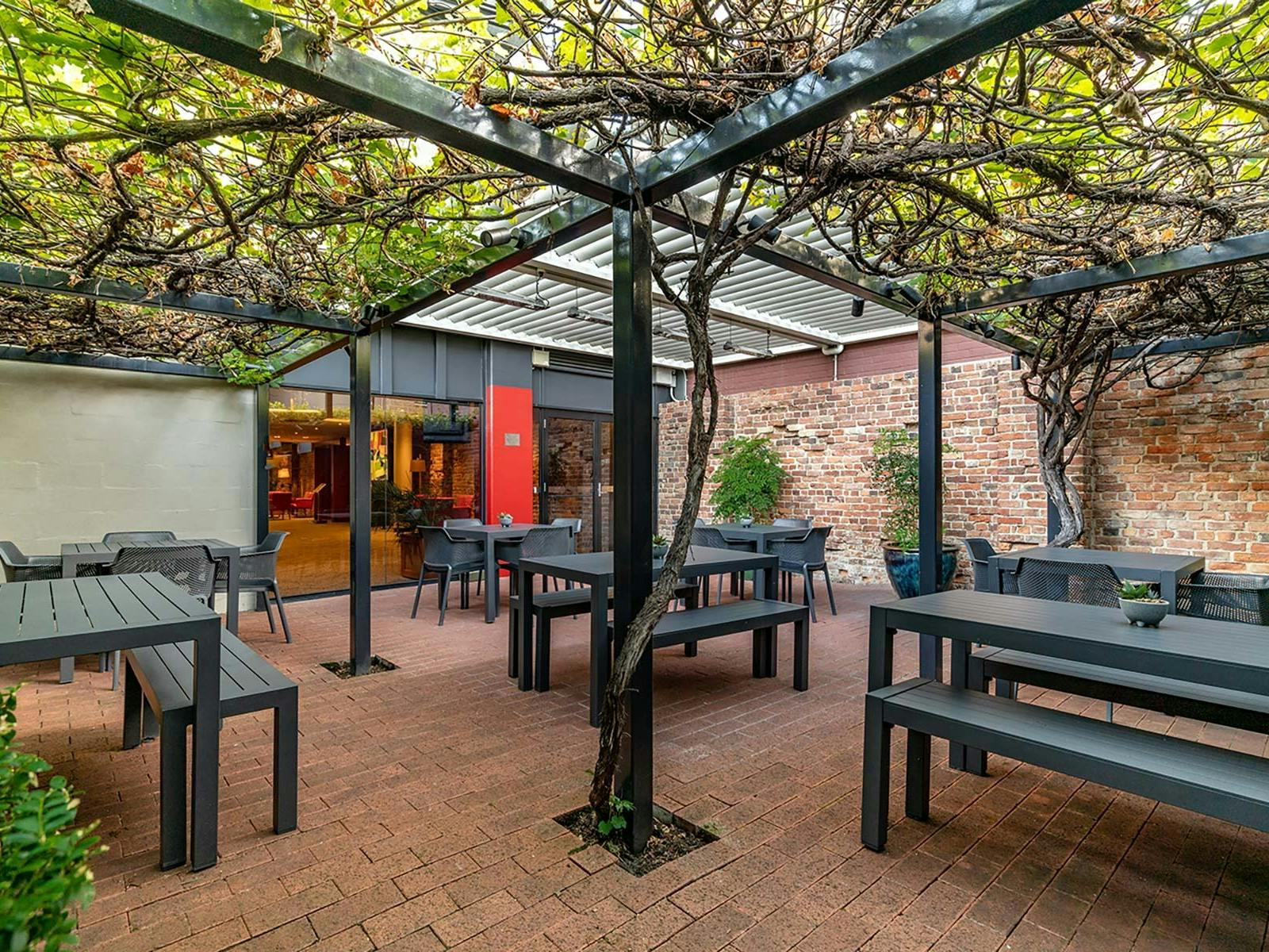 Outdoor brick courtyard. Pergola like structure covered in lush green vines.