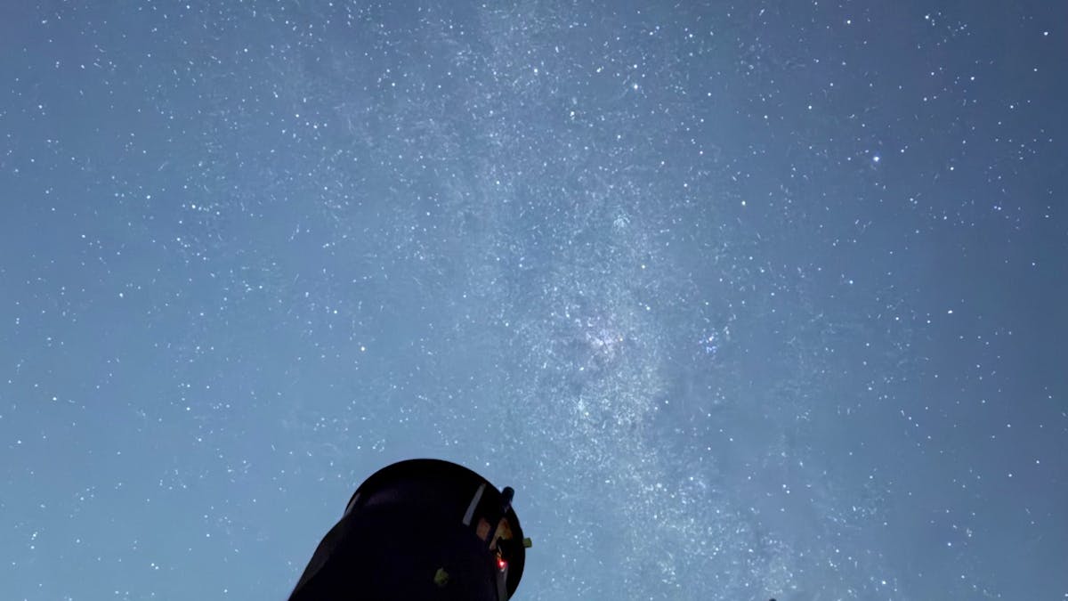 Massive 30" telescope pointing to the milky way sky, with a ladder on the side for viewing