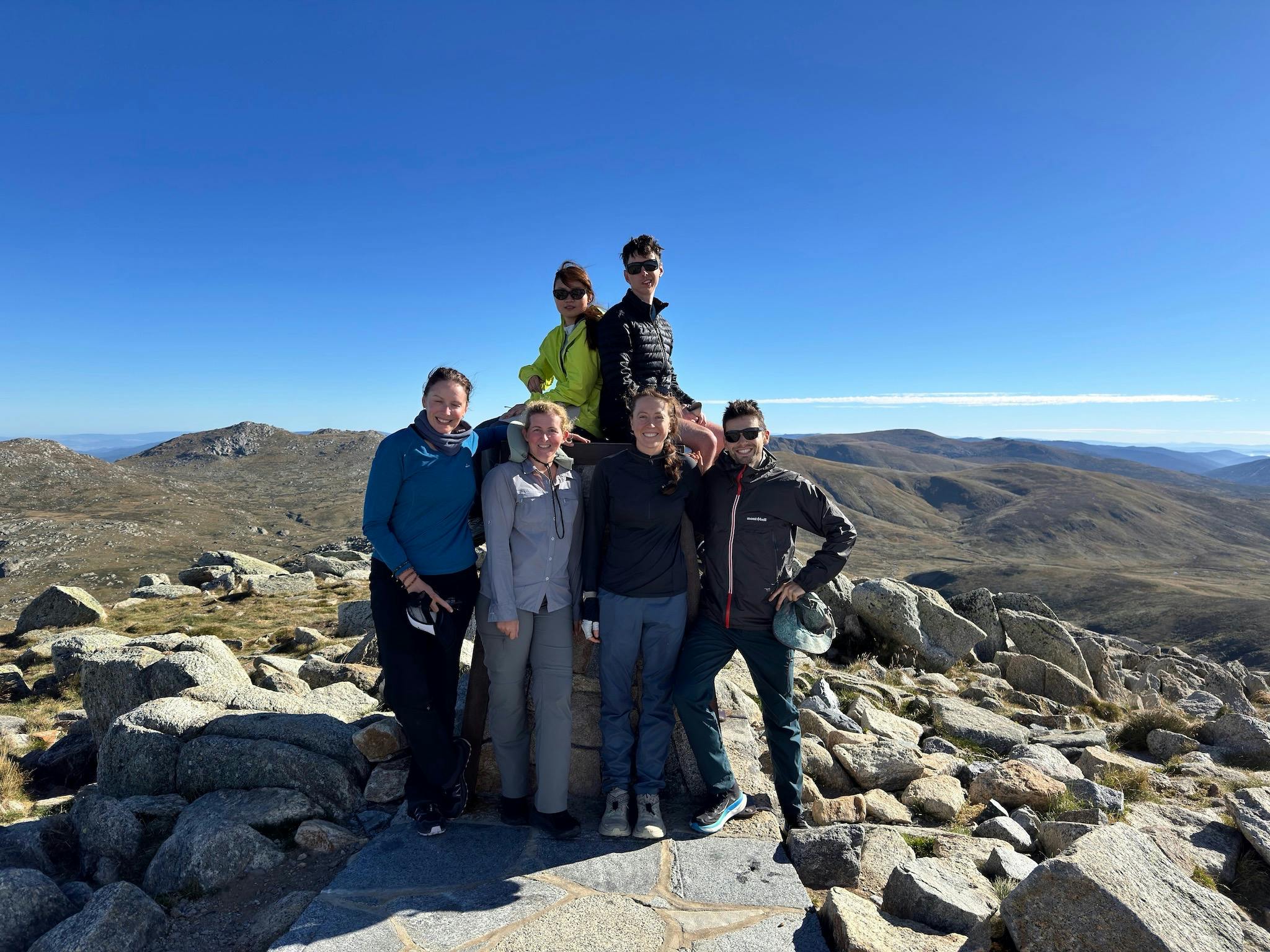 Six hikers at the top of a mountain with some blue skies
