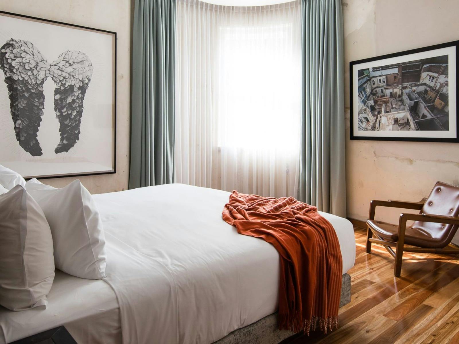A light-filled bedroom with warm timber floors and a large white bed.