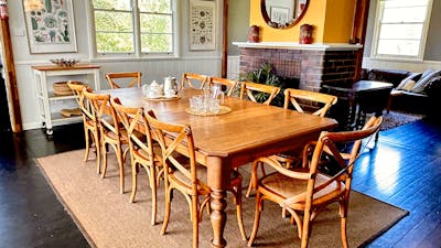 Large dining table on rug with fireplace behind, art, mirror, daylight in windows