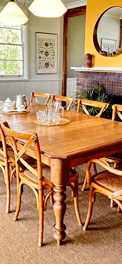 Large dining table on rug with fireplace behind, art, mirror, daylight in windows