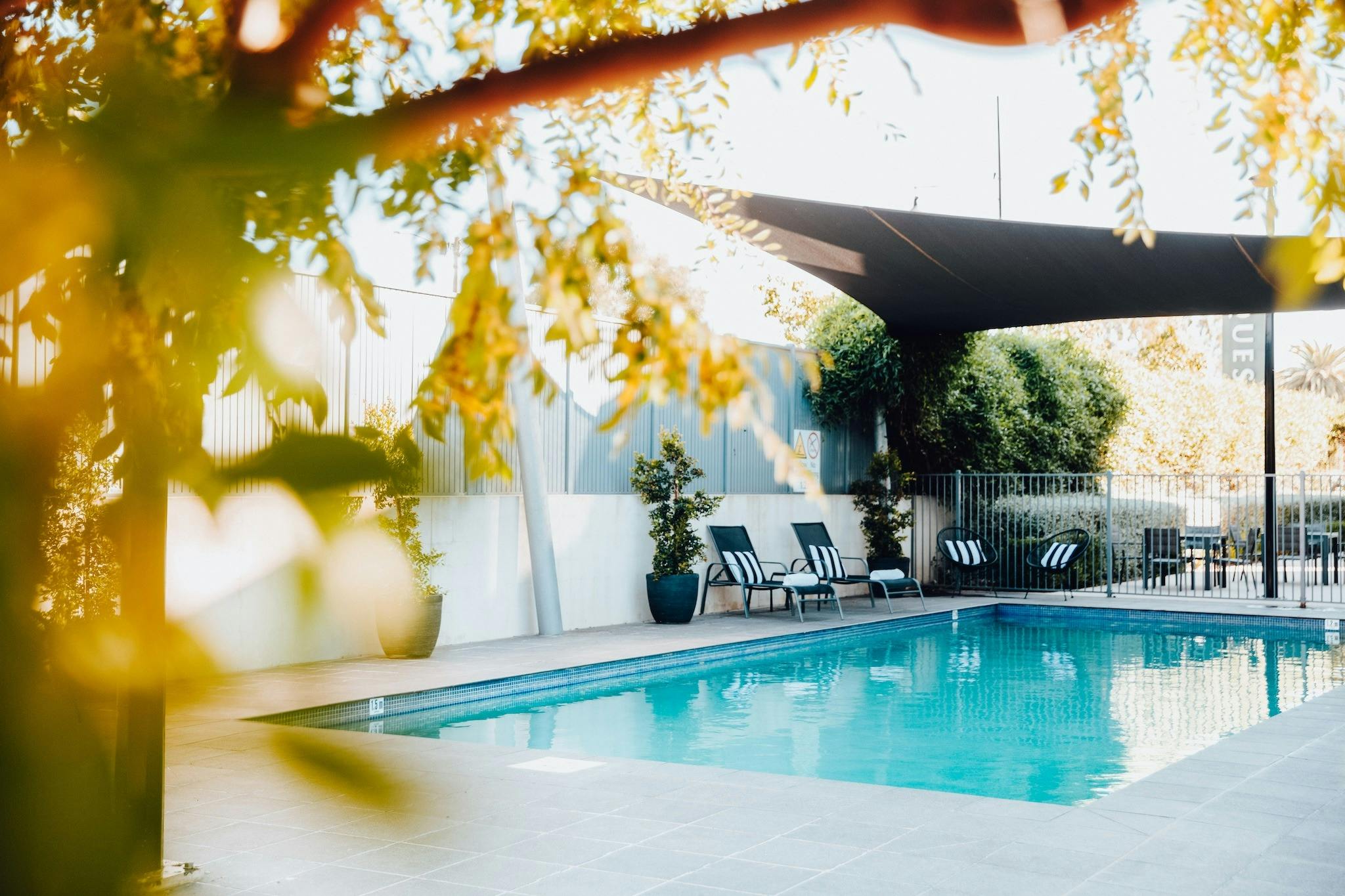 Outdoor pool area surrounded by greenery and shaded from the sun