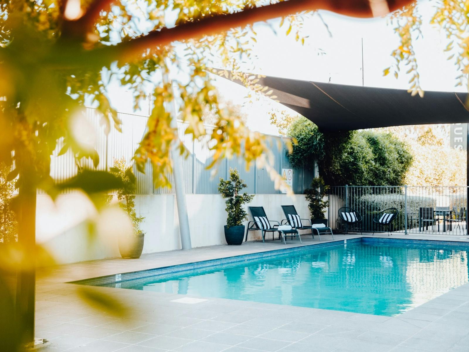 Outdoor pool area surrounded by greenery and shaded from the sun