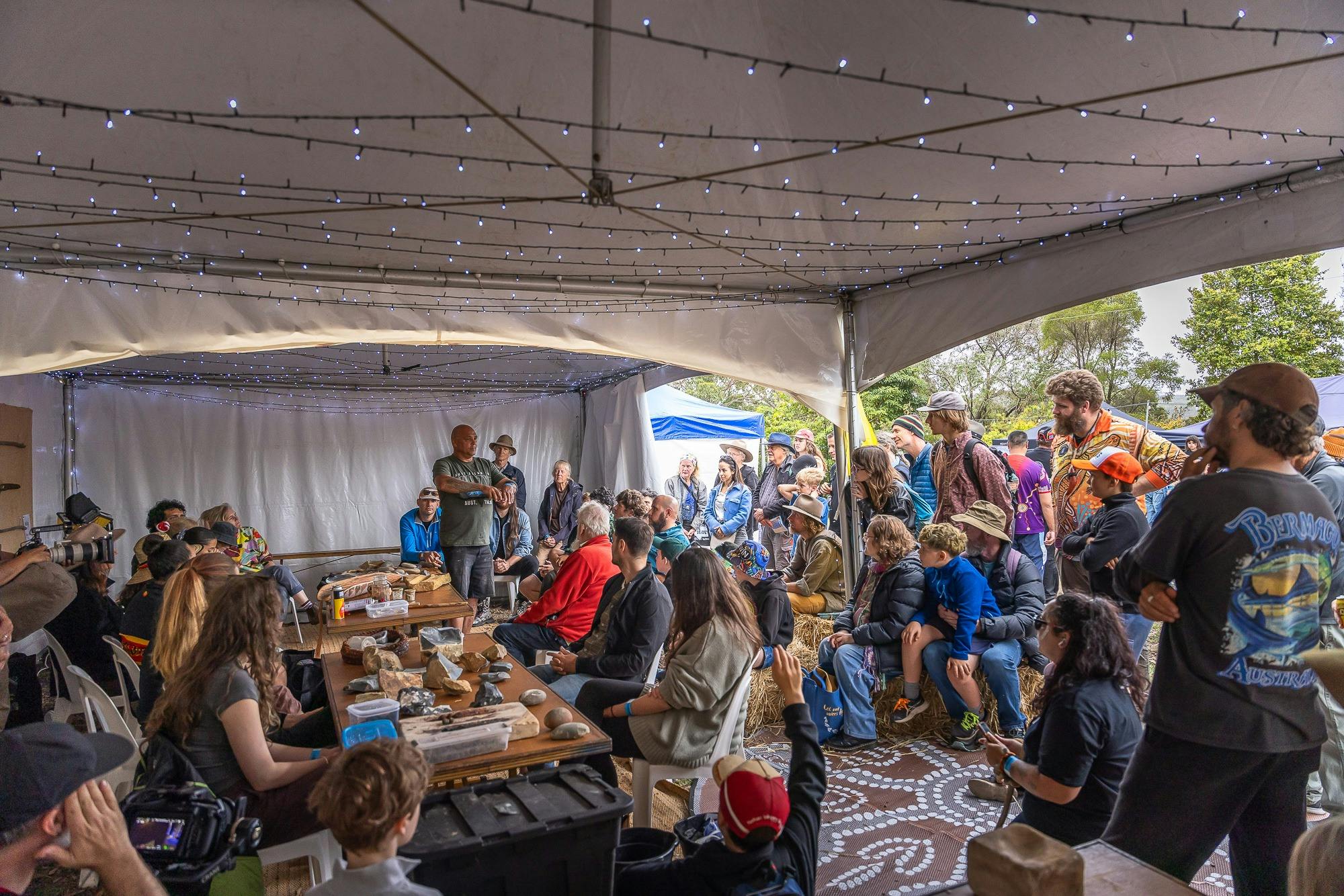 An Aboriginal man presents a workshop on stone tools to a large crowd in a marquee