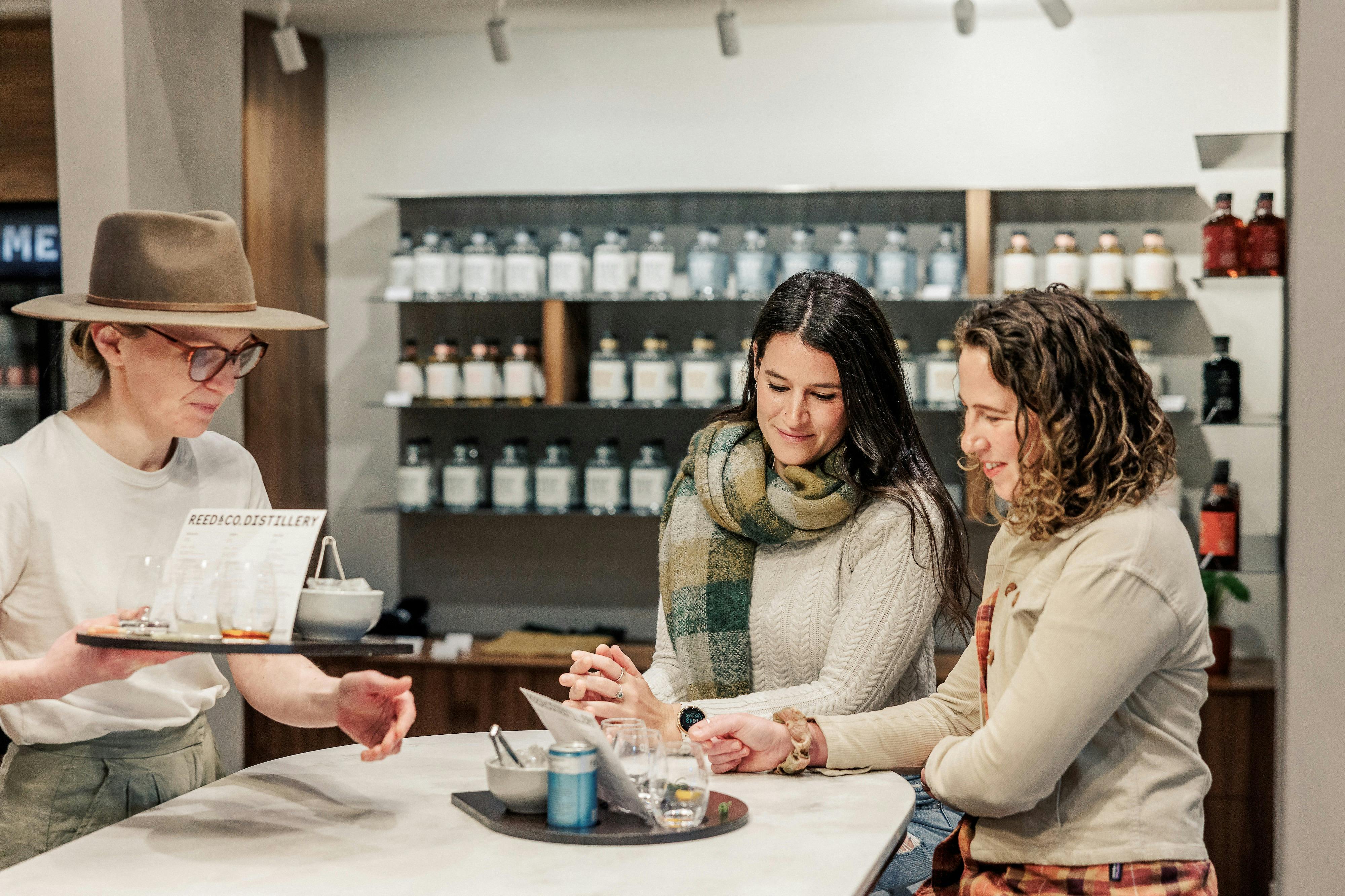 Two guests sit at a bar tasting drinks served by a staff member