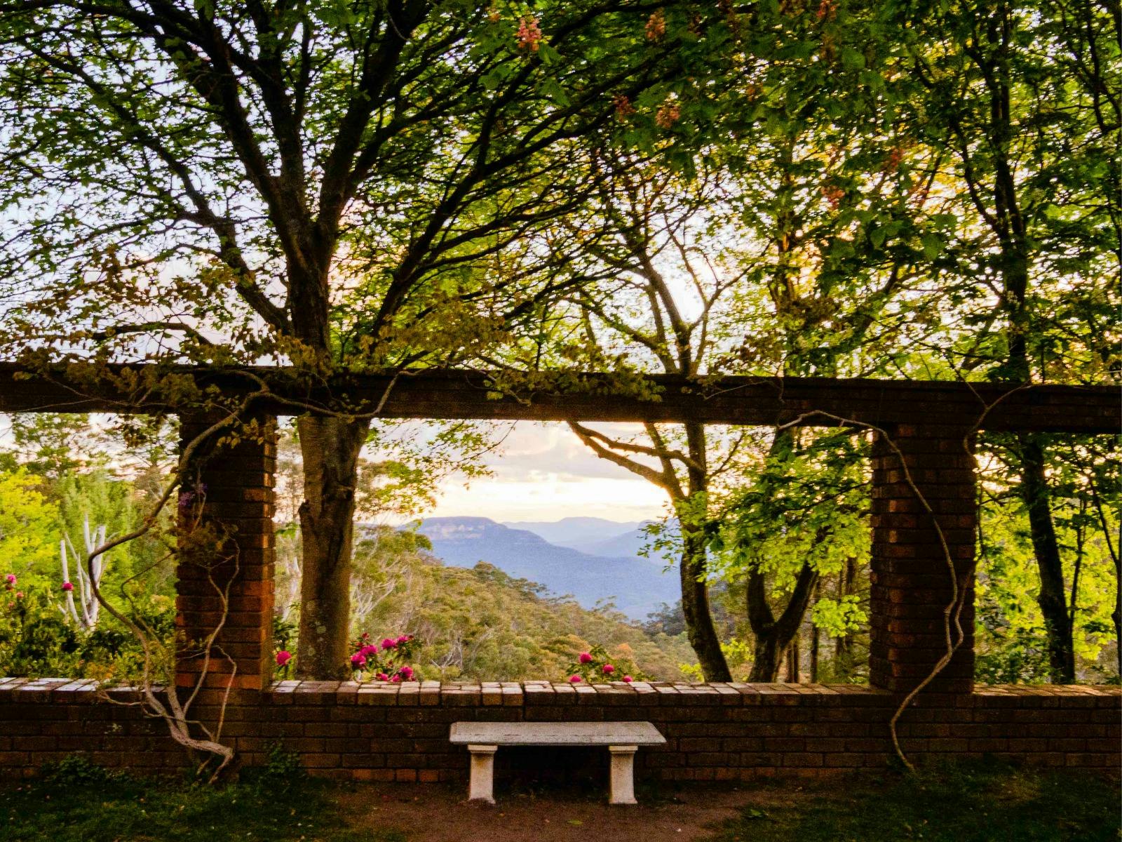 The sun sets over the Blue Mountains. The view is seen beyond a brick wall.