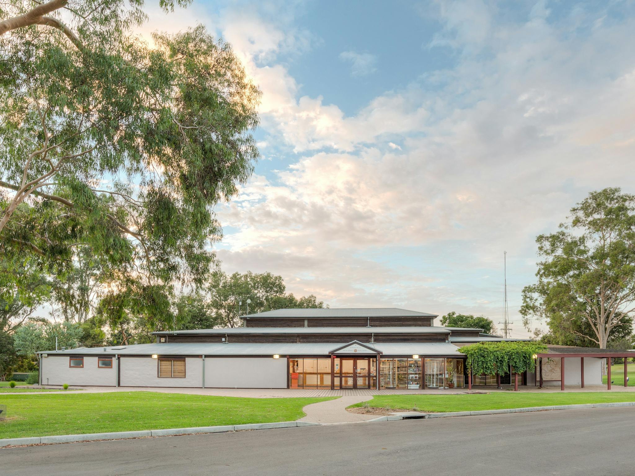 A  wideangled shot of the gallery with the deck area, lawns and lemon scented gum in the foreground.