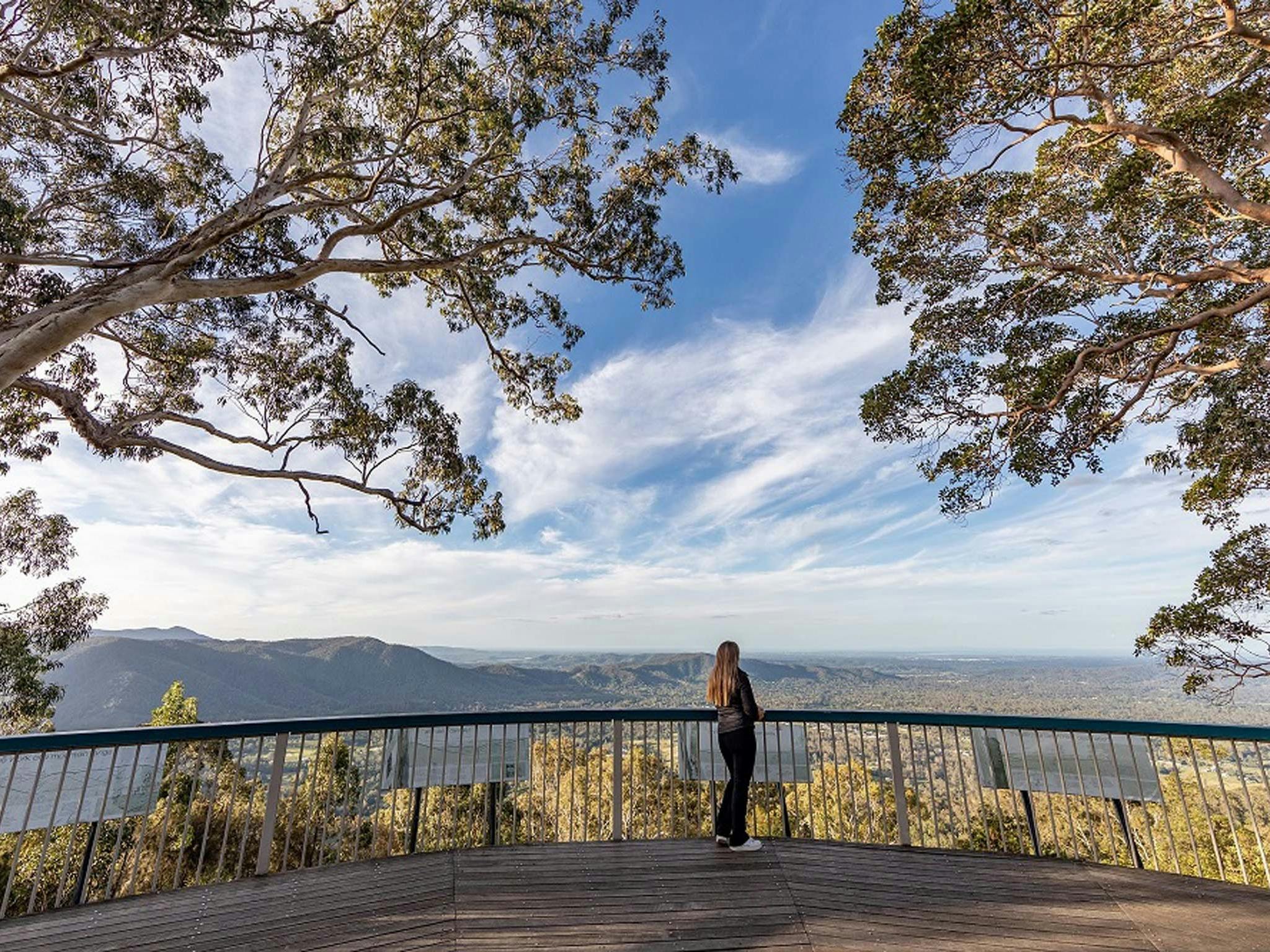 Woman standing on a deck looking at view of mountains and valley Woman standing on a deck looking at view of mountains and valley