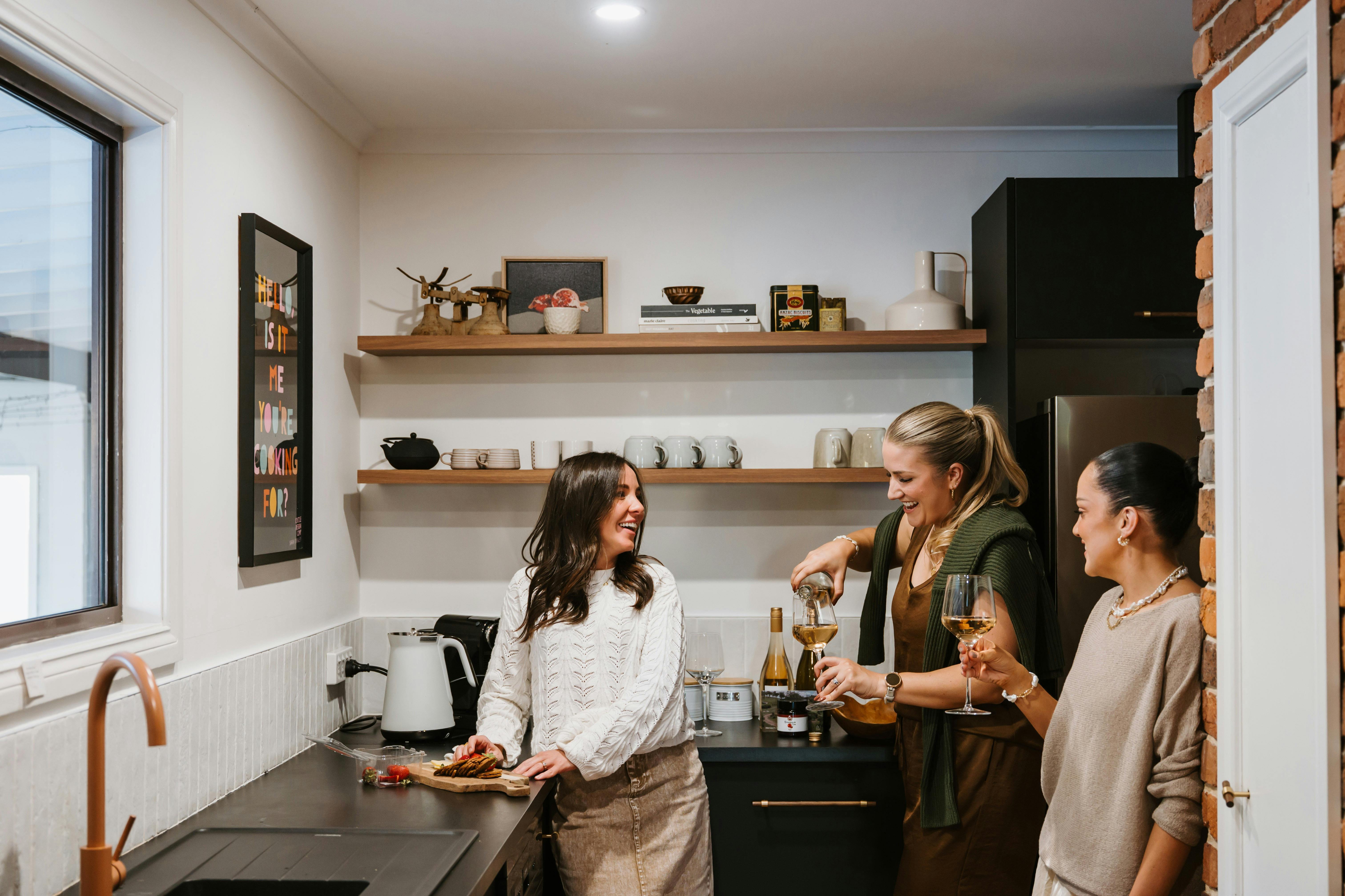 Women preparing a cheese board in Wandarra's kitchen and pouring a glass of wine