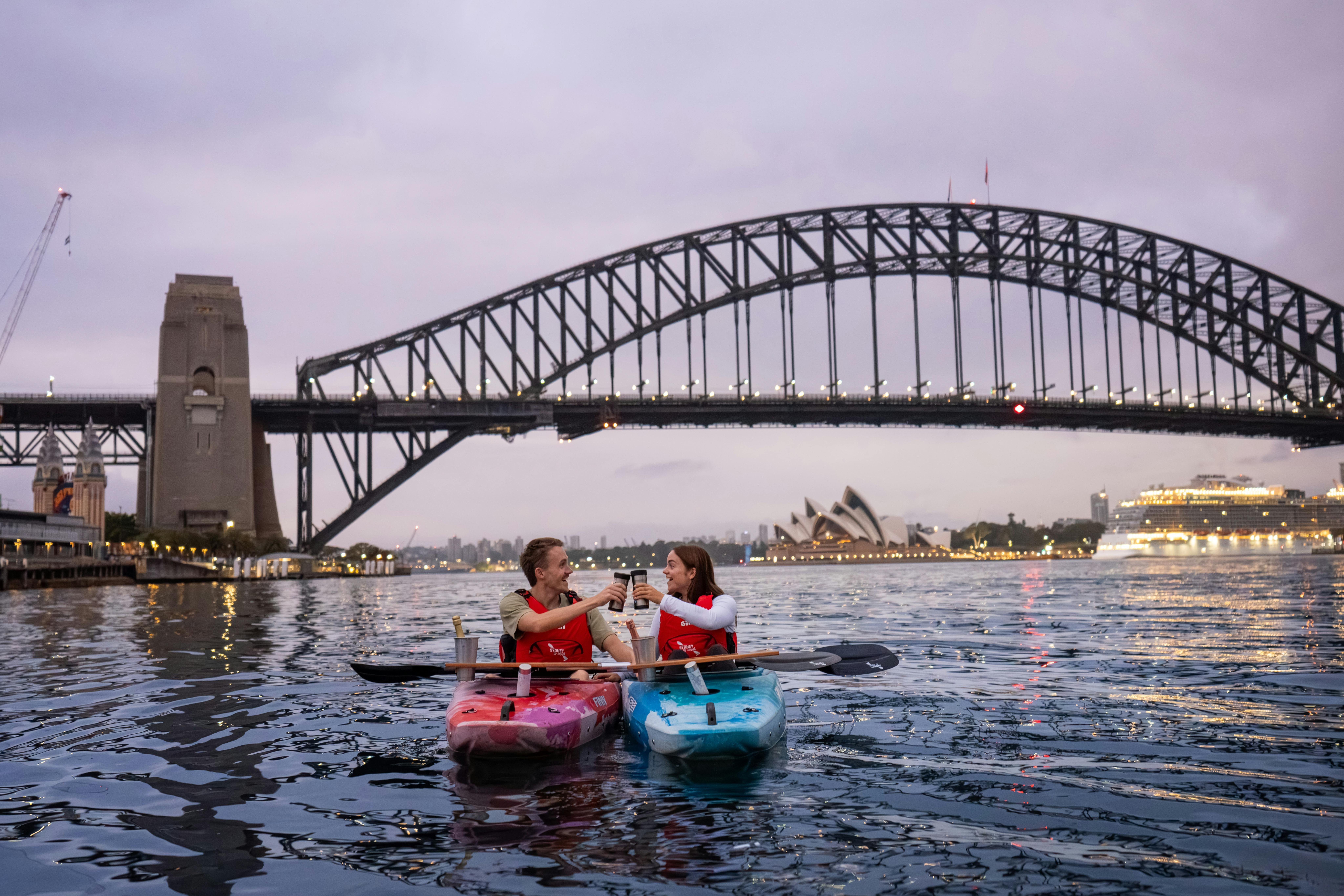 Romantic couple cheers coffees from their kayaks with views of Sydney Harbour Bridge and Opera House