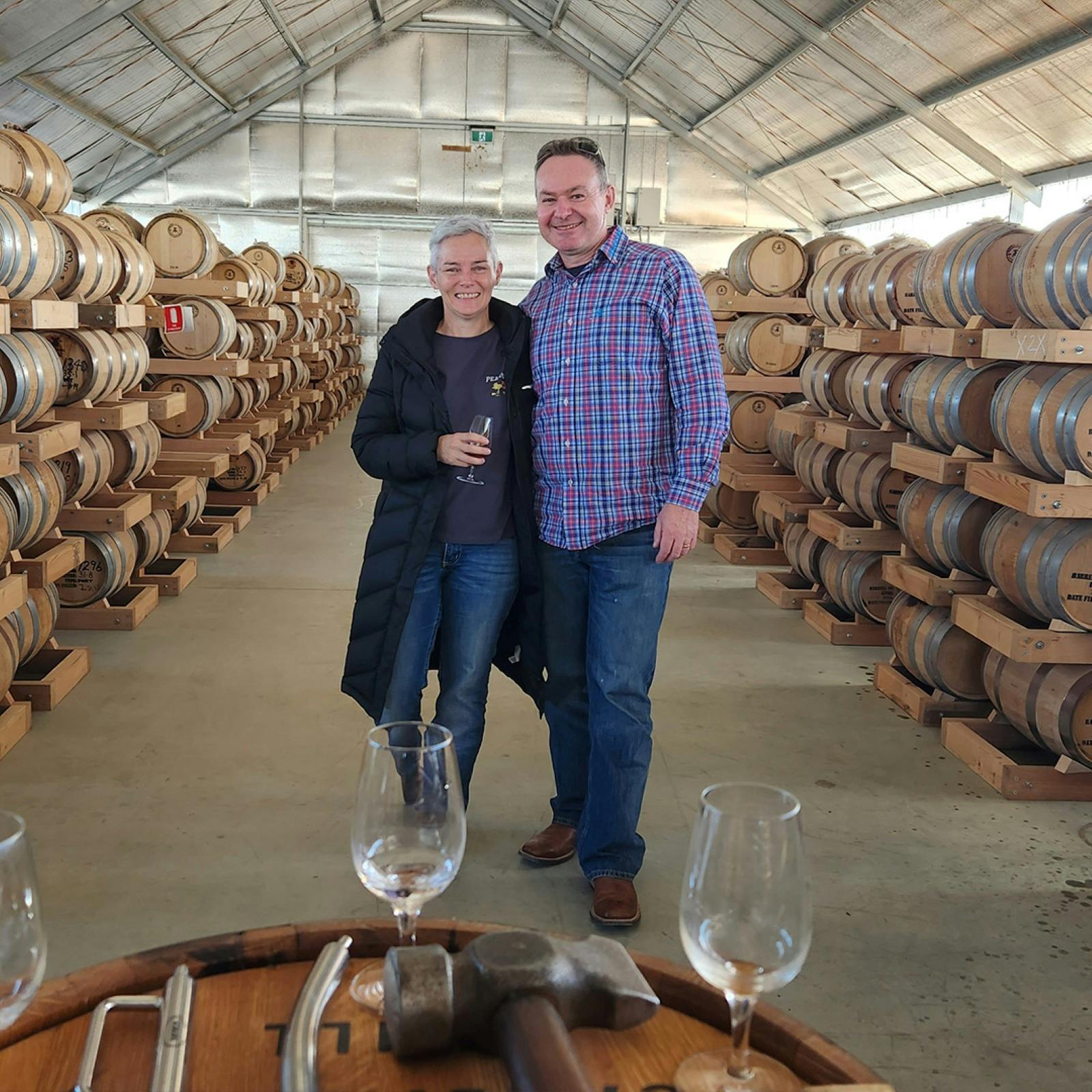Two people standing in a shed surrounded by whisky casks