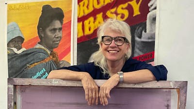 A woman with blonde hair and glasses leaning on a purple artwork piece.
