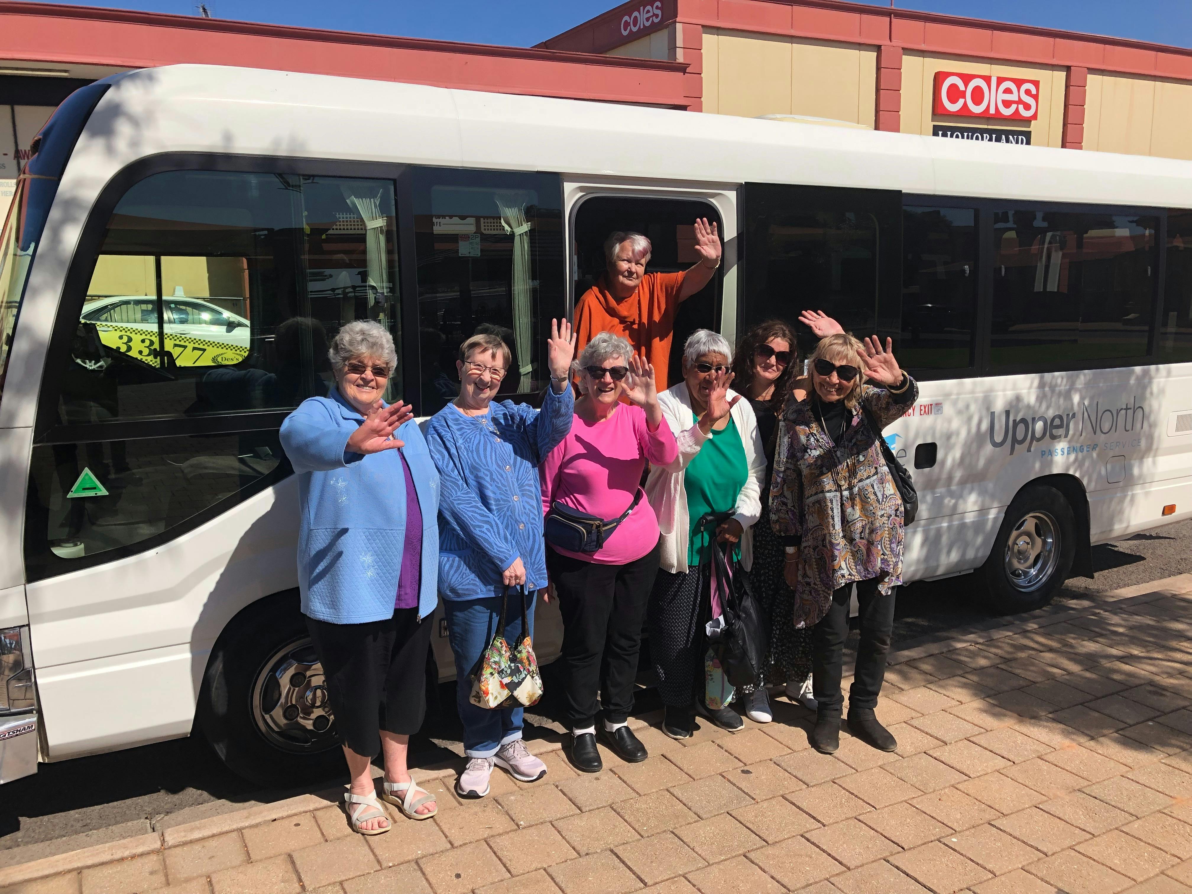 Small group of people standing in front of bus and waving