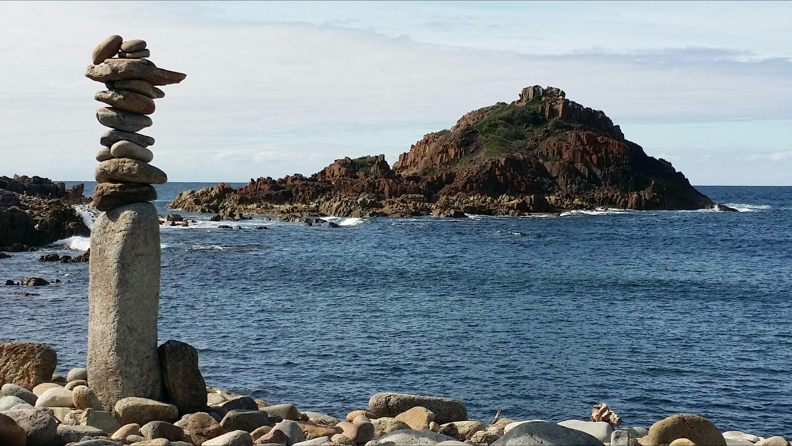 rock cairn sculpture beside the ocean with small island in background