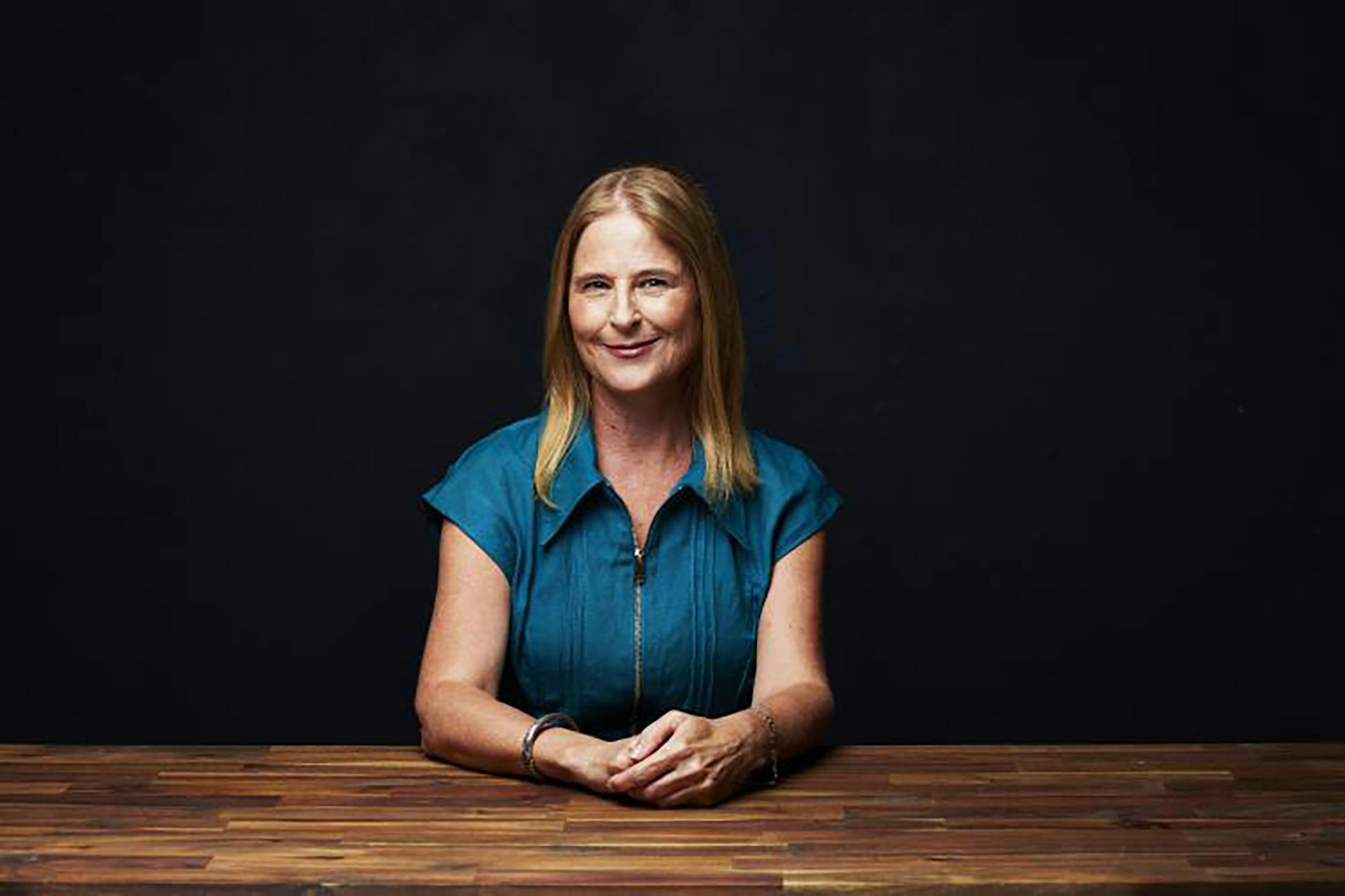 A woman smiling in a blue shirt at a wooden table