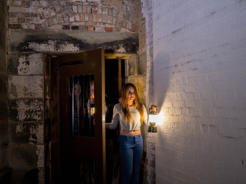 a young woman emerges from a darkened cell holding a lantern from bar