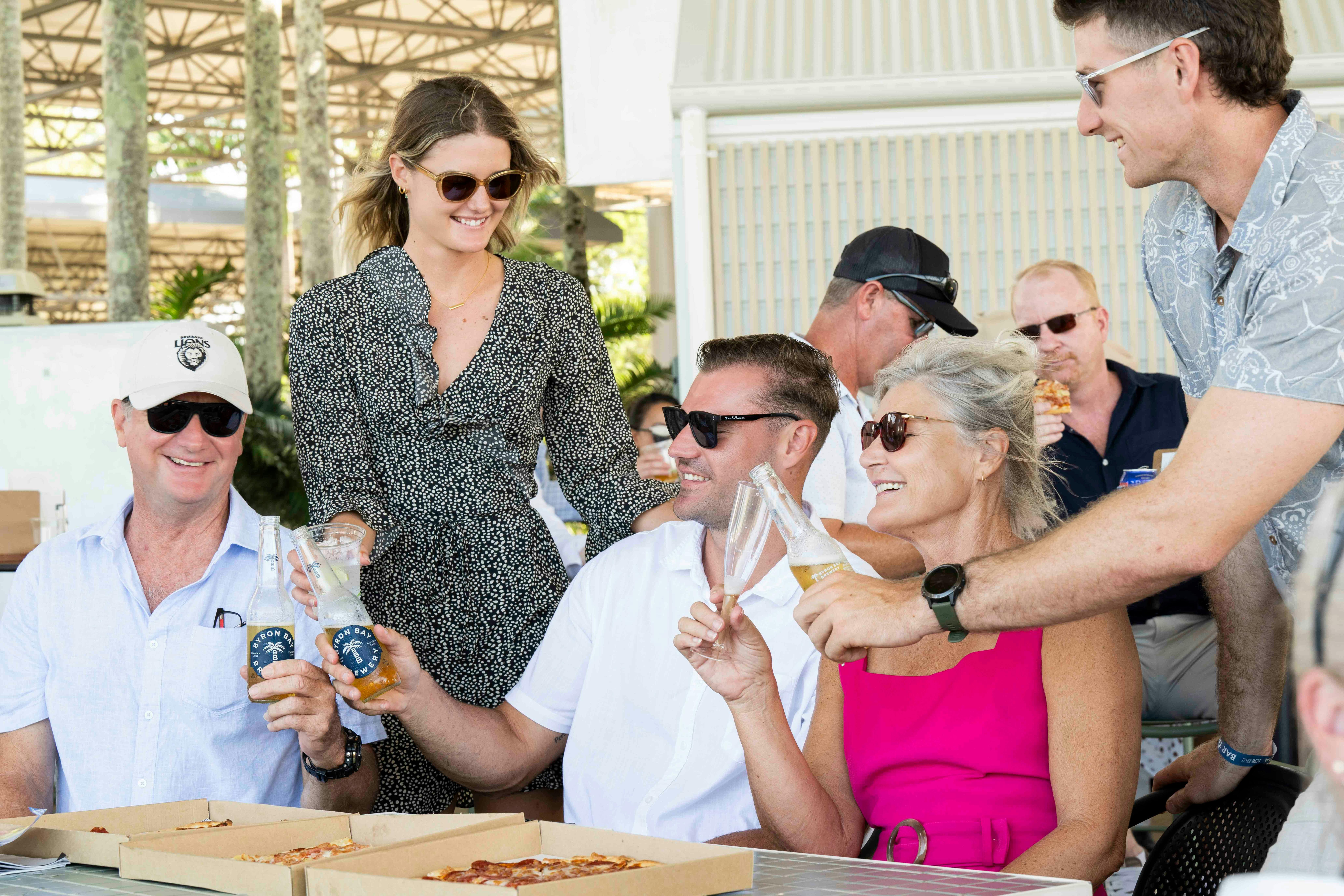 Family cheers beers with pizzas on the table in an outdoor setting