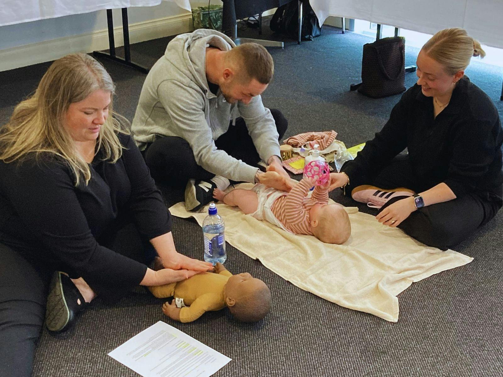 Infant massage instructor demonstrating while a father massages his baby and mother watches.