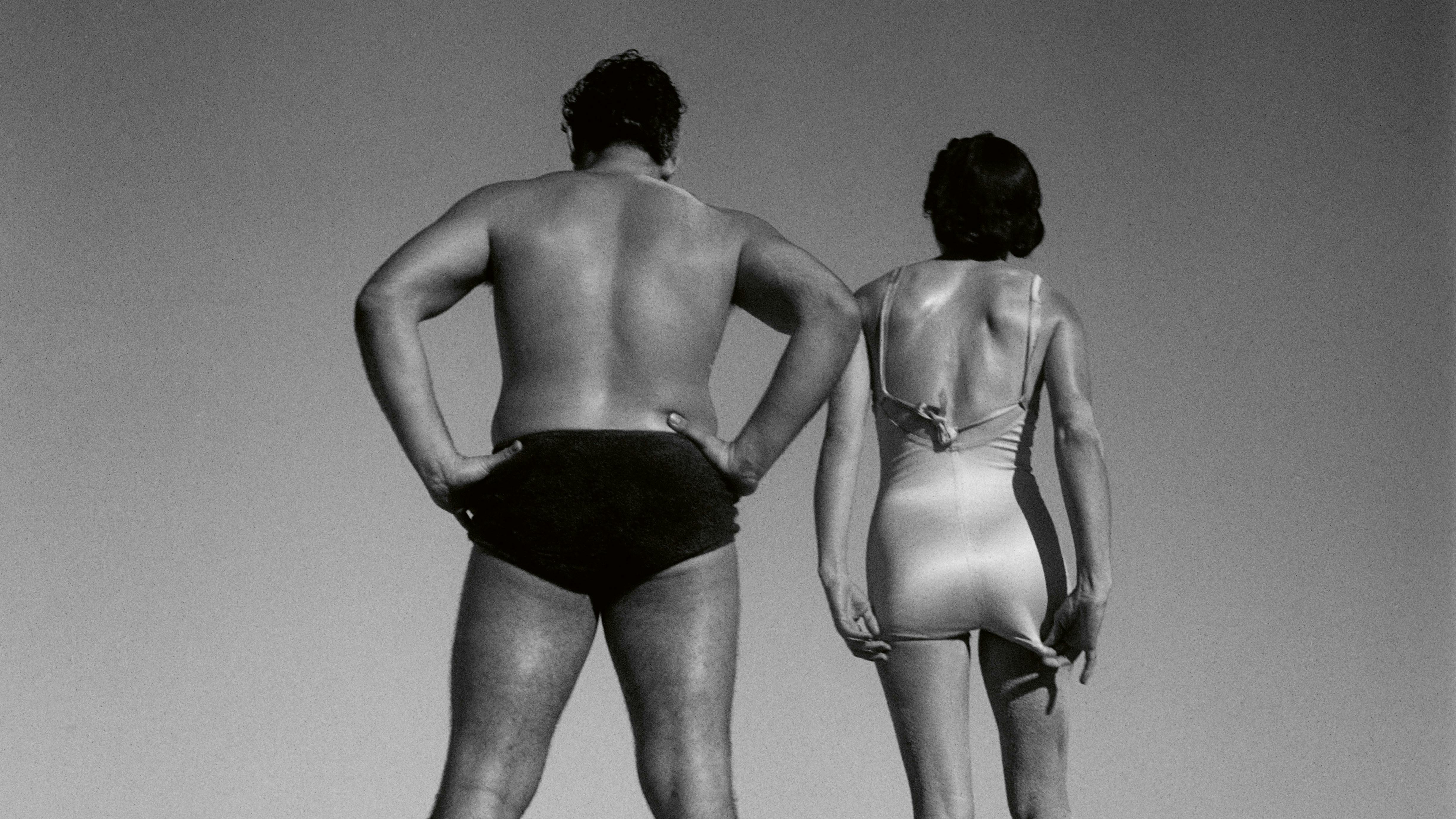 A black and white photo of the back of two people in swimwear