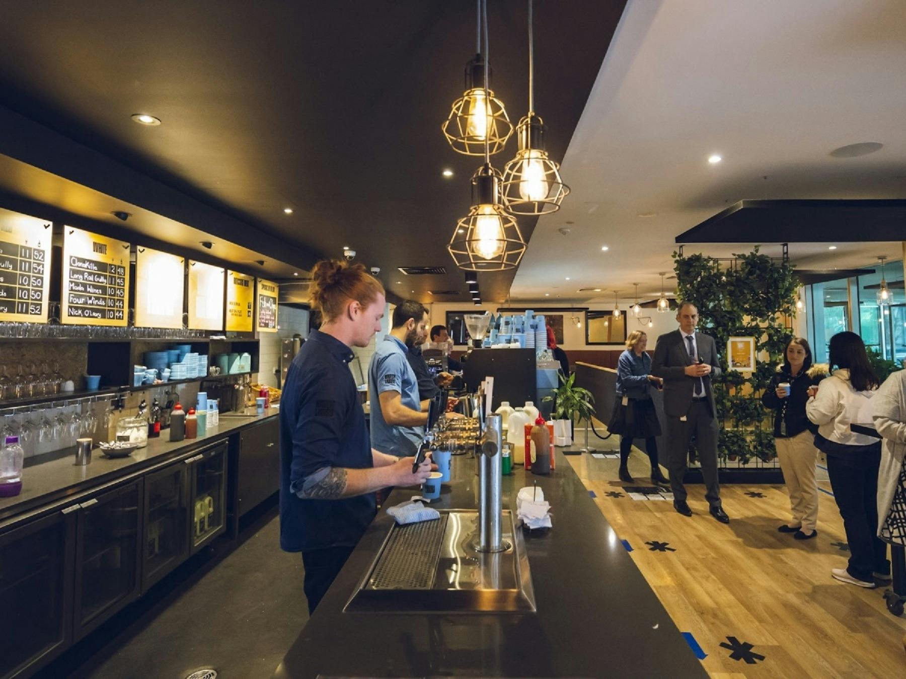 Wait staff serving drinks behind the bar with customers waiting to collect  drinks