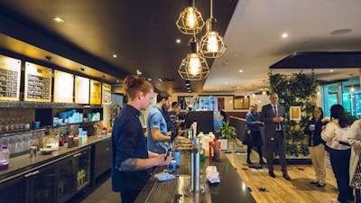 Wait staff serving drinks behind the bar with customers waiting to collect  drinks