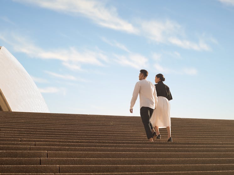 A couple climbs the steps of the Sydney Opera House
