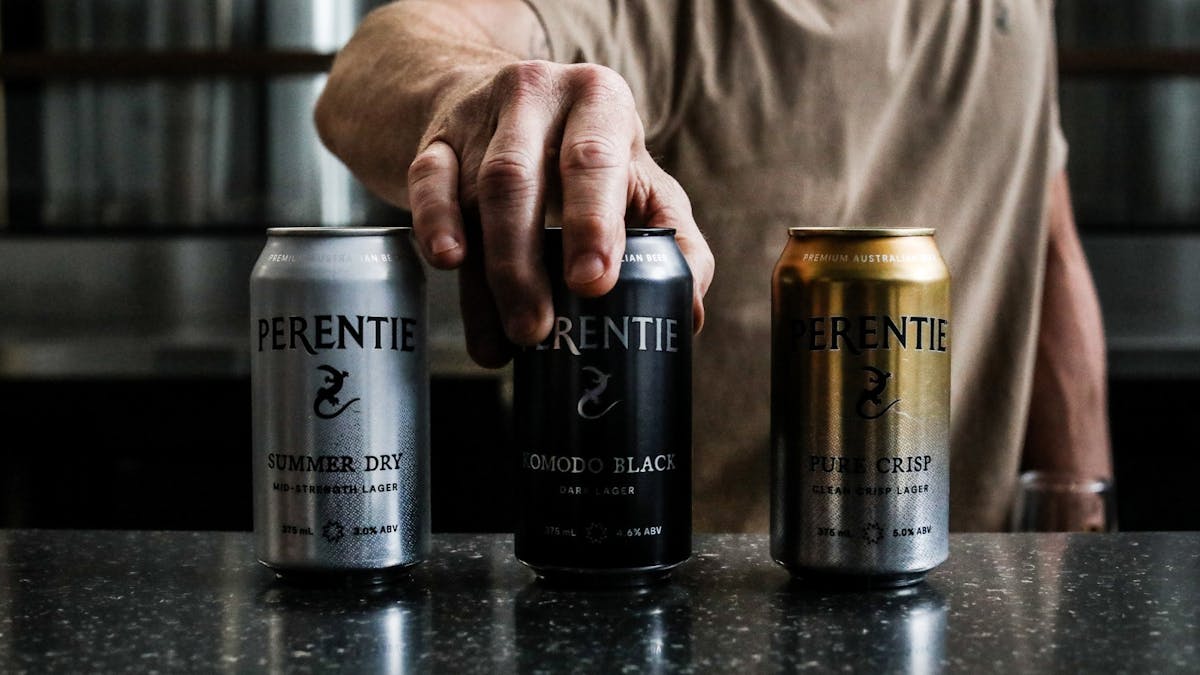 male hand holding a can in the middle of a row of three beer cans with Perentie branding