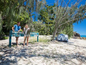 Smiling couple standing at a Hook Island, Steen Beach sign with a camping tent nearby