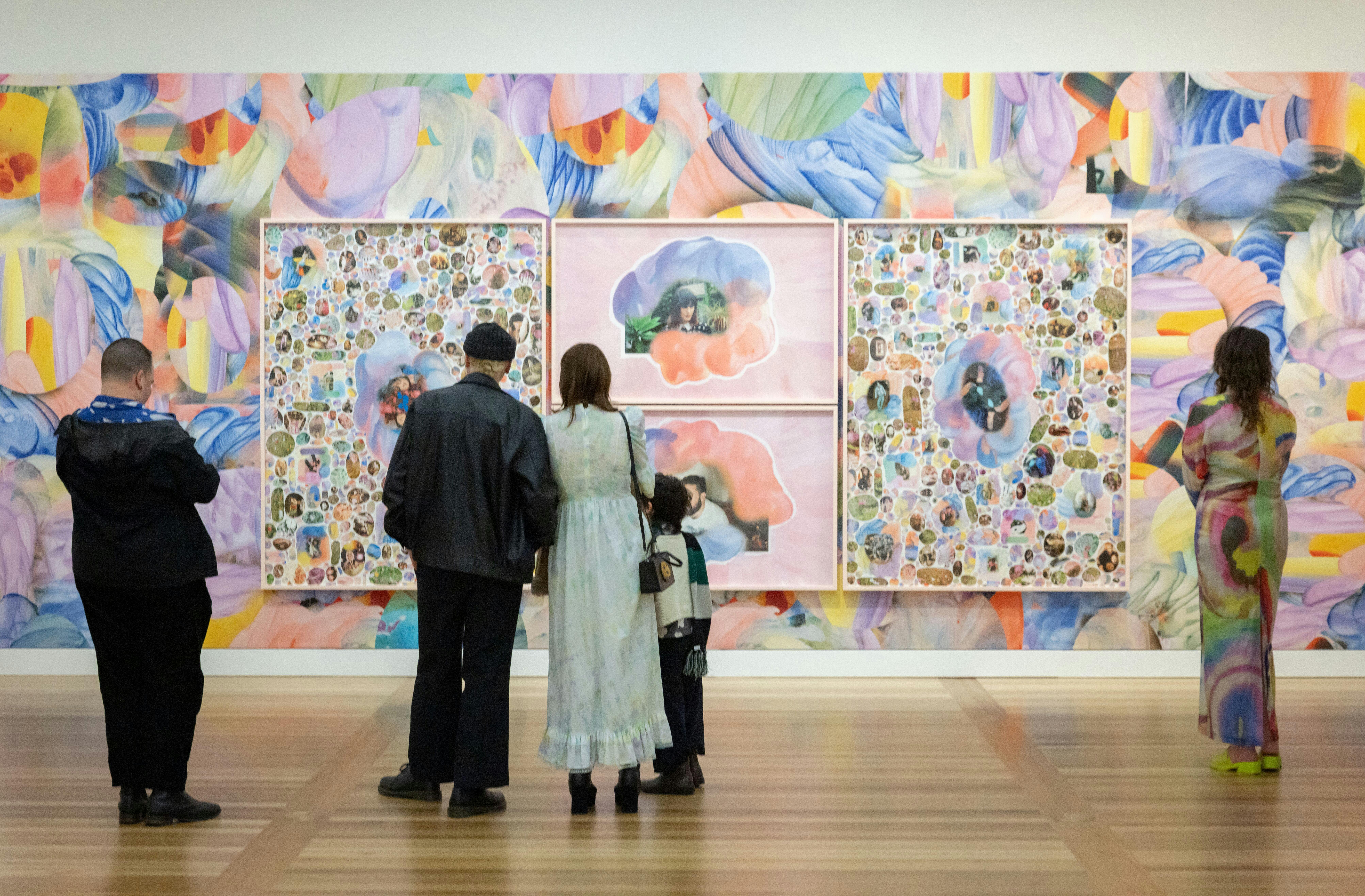 Five people look at a vibrant portrait collage upon a colourful wall.